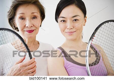 Stock Image - Japanese mother and daughter holding tennis racquet. Fotosearch