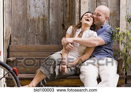 Stock Image - Laughing couple hugging on bench. Fotosearch
