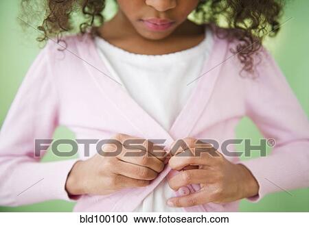 Stock Image - Mixed race girl buttoning sweater. Fotosearch