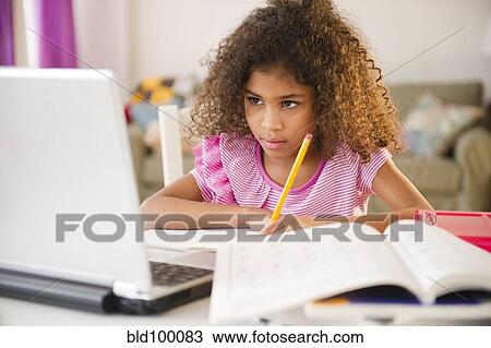 Stock Image - Mixed race girl doing homework with laptop. Fotosearch