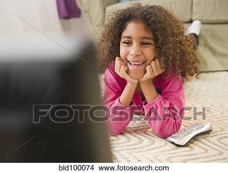 Picture - Mixed race girl laying on floor watching television. Fotosearch