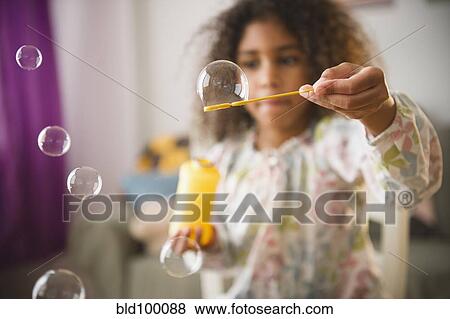 Stock Photo - Mixed race girl playing with bubbles. Fotosearch