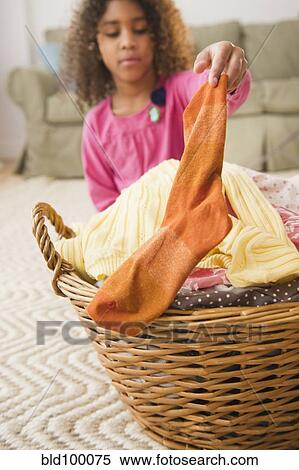Stock Photography - Mixed race girl putting sock into laundry basket. Fotosearch