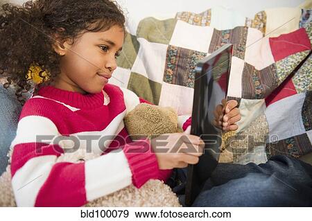 Mixed race girl sitting on sofa using digital tablet View Large Photo Image Stock Photo - Mixed race girl sitting on sofa using digital tablet. Fotosearch