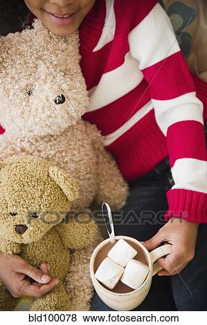 Stock Photo - Mixed race girl with teddy bears drinking hot chocolate. Fotosearch