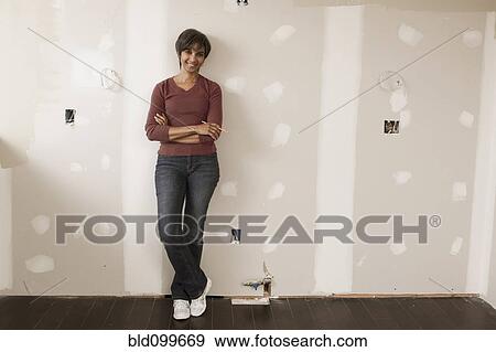 Stock Photo - Mixed race woman leaning on wall in unfinished room. Fotosearch
