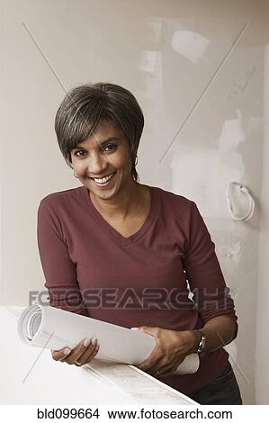 Mixed race woman standing in unfinished room with blueprints View Large Photo Image Picture - Mixed race woman standing in unfinished room with blueprints. Fotosearch