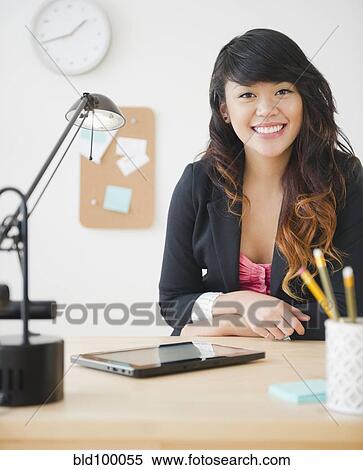 Stock Photography - Pacific Islander businesswoman sitting at desk with digital tablet. Fotosearch