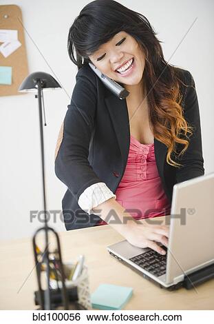 Stock Photograph - Pacific Islander businesswoman using laptop and talking on telephone. Fotosearch