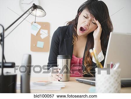 Stock Photo - Pacific Islander businesswoman yawning at desk. Fotosearch