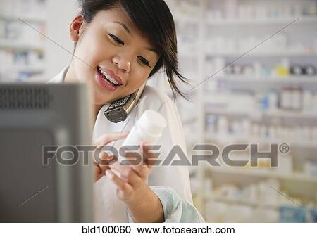 Stock Image - Pacific Islander pharmacist reviewing medication and talking on telephone. Fotosearch