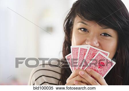 Stock Photography - Pacific Islander woman covering her mouth with playing cards. Fotosearch