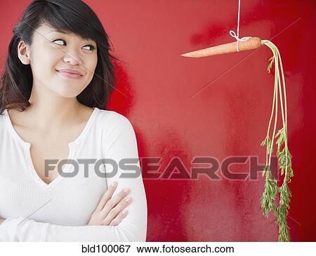 Stock Photo - Pacific Islander woman looking at a carrot on a string. Fotosearch