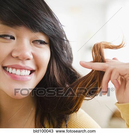 Stock Image - Pacific Islander woman looking at her hair. Fotosearch