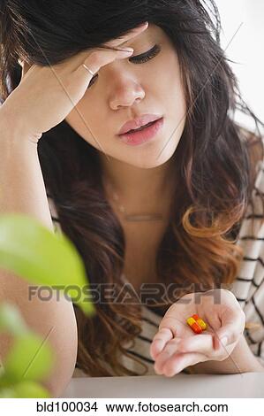 Picture - Pacific Islander woman looking at pills in her hand. Fotosearch