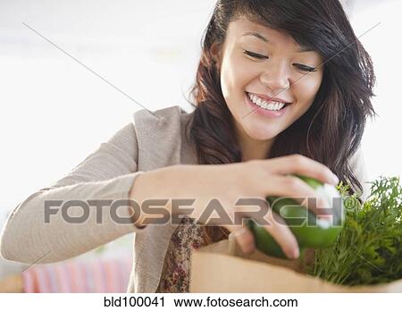 Stock Image - Pacific Islander woman taking groceries from grocery bag. Fotosearch