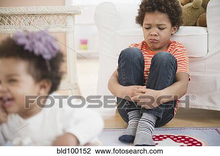 Stock Image - Sad Black boy sitting in living room. Fotosearch
