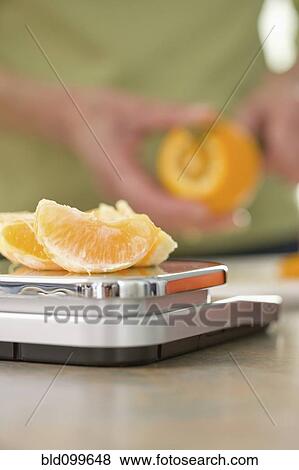 Stock Photo - Senior woman weighing orange on scale. Fotosearch