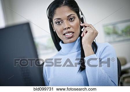 Stock Image - Serious businesswoman working at desk in headset. Fotosearch