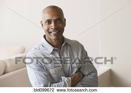 Stock Image - Smiling African American man standing in unfinished room. Fotosearch