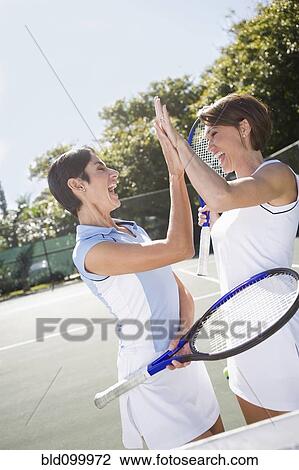 Stock Image - Women high-fiving after a game of doubles tennis. Fotosearch