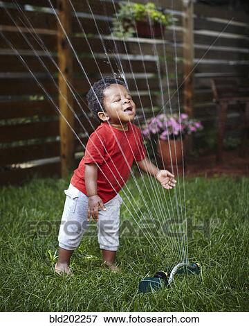 Stock Photo - African American baby playing in sprinkler. Fotosearch