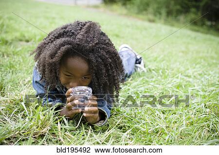 Stock Image - African American boy laying in grass and looking in jar. Fotosearch