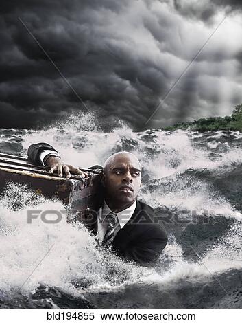 Stock Photography - African American businessman in ocean holding trunk. Fotosearch
