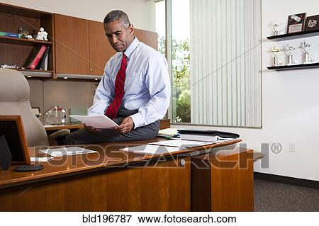 Stock Photo - African American businessman sitting on desk. Fotosearch