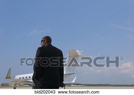 Stock Image - African American businessman standing on airport tarmac. Fotosearch