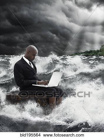 Picture - African American businessman using laptop in stormy sea. Fotosearch