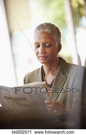 Stock Image - African American businesswoman reading newspaper in cafe. Fotosearch