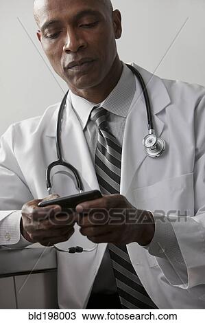 Stock Image - African American doctor text messaging on cell phone. Fotosearch