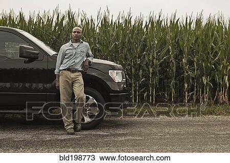 Stock Image - African American farmer leaning on car next to crop. Fotosearch