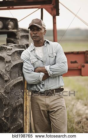 Stock Photography - African American farmer standing near tractor. Fotosearch