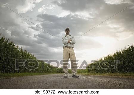 Stock Image - African American farmer standing on road through crops. Fotosearch