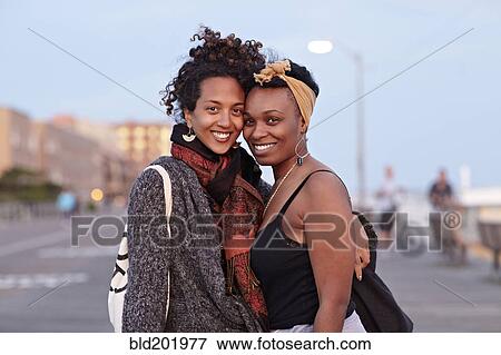 Stock Photo - African American friends hugging on sidewalk. Fotosearch