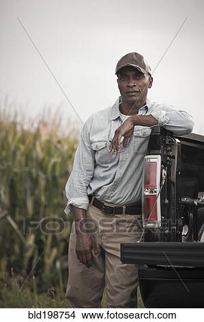 Picture - African American leaning on back of pick-up truck. Fotosearch