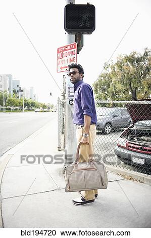 Stock Image - African American man carrying bag on sidewalk. Fotosearch