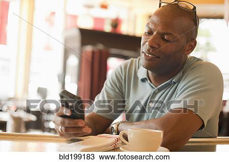 Stock Image - African American man in restaurant text messaging on cell phone. Fotosearch
