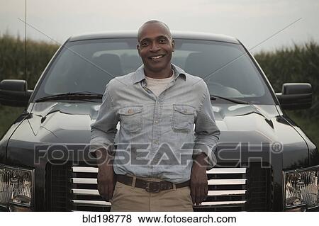 Stock Photo - African American man leaning on hood of car. Fotosearch