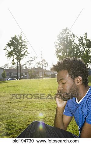 Stock Image - African American man sitting outdoors using cell phone. Fotosearch