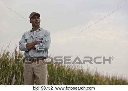 Stock Image - African American man standing in field with arms crossed. Fotosearch