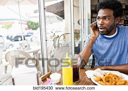 Stock Image - African American man talking on cell phone in diner. Fotosearch