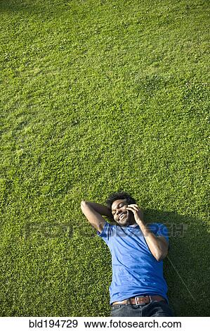 Stock Photo - African American man using cell phone laying on grass. Fotosearch