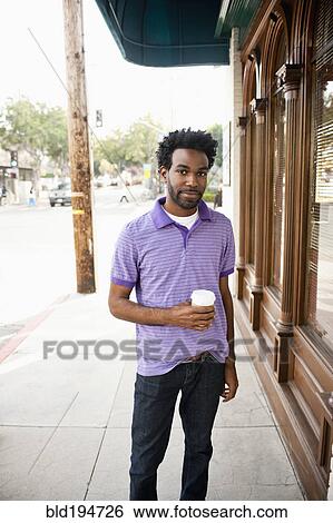 Stock Photograph - African American man with coffee cup standing on sidewalk. Fotosearch