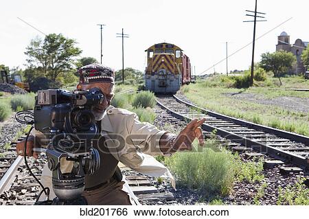 Stock Photograph - African American man with film camera near railroad tracks. Fotosearch