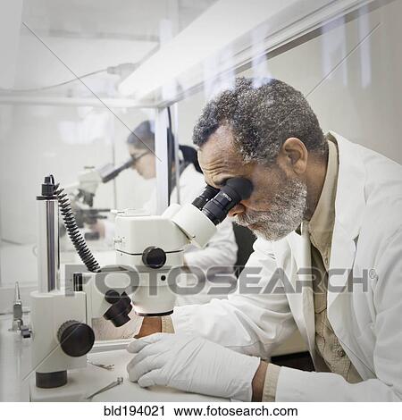 Stock Image - African American scientist using microscope in laboratory. Fotosearch