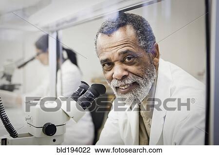 Stock Image - African American scientist using microscope in laboratory. Fotosearch