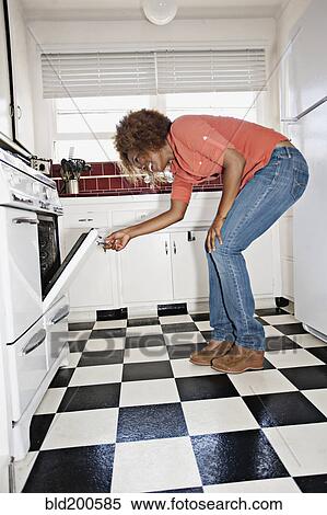 Stock Photography - African American woman looking in oven. Fotosearch